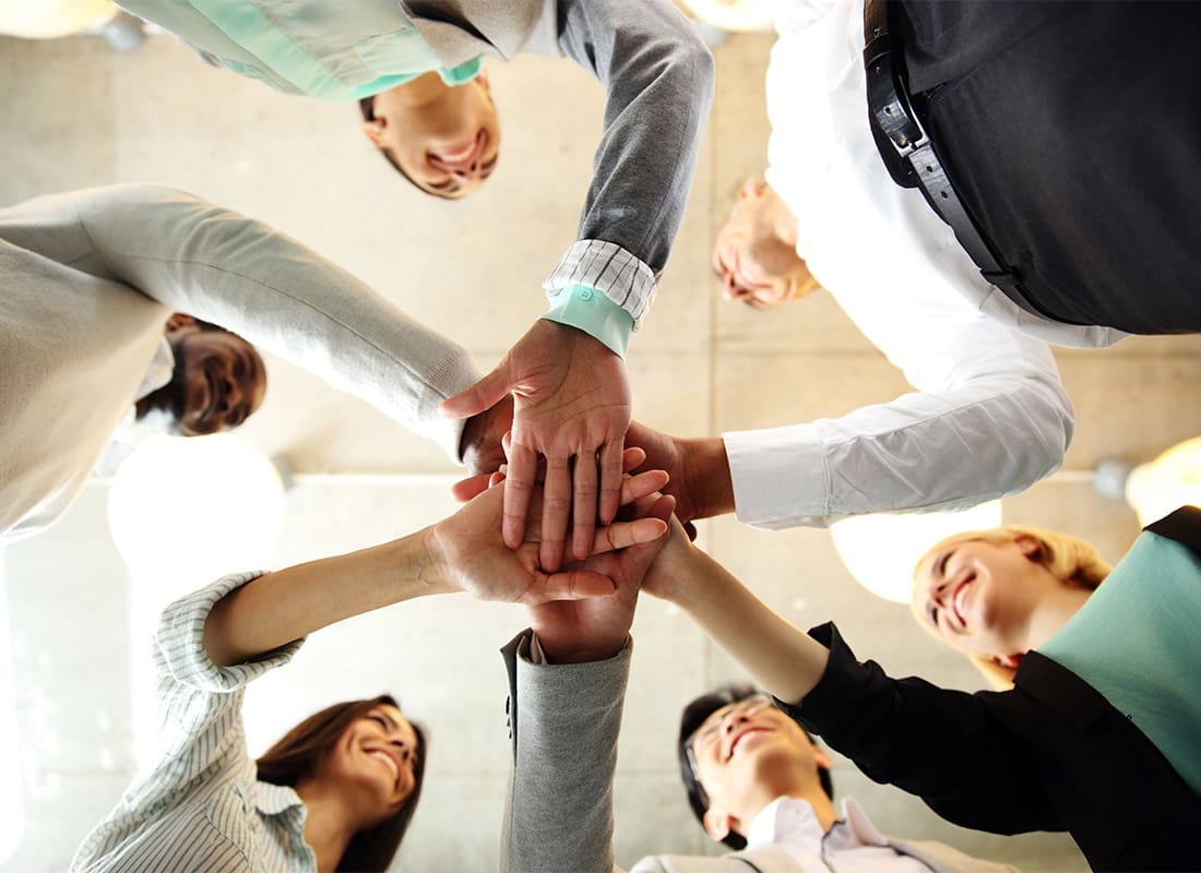 About Our Agency - View Looking Up at a Small Group of Smiling Employees Standing in a Circle with Their Hands Together