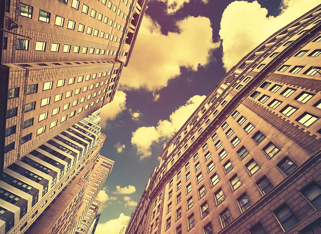 Insurance Solutions - Vintage Toned View Looking Up at Tall Brick Buildings in a City with a Cloudy Blue Sky